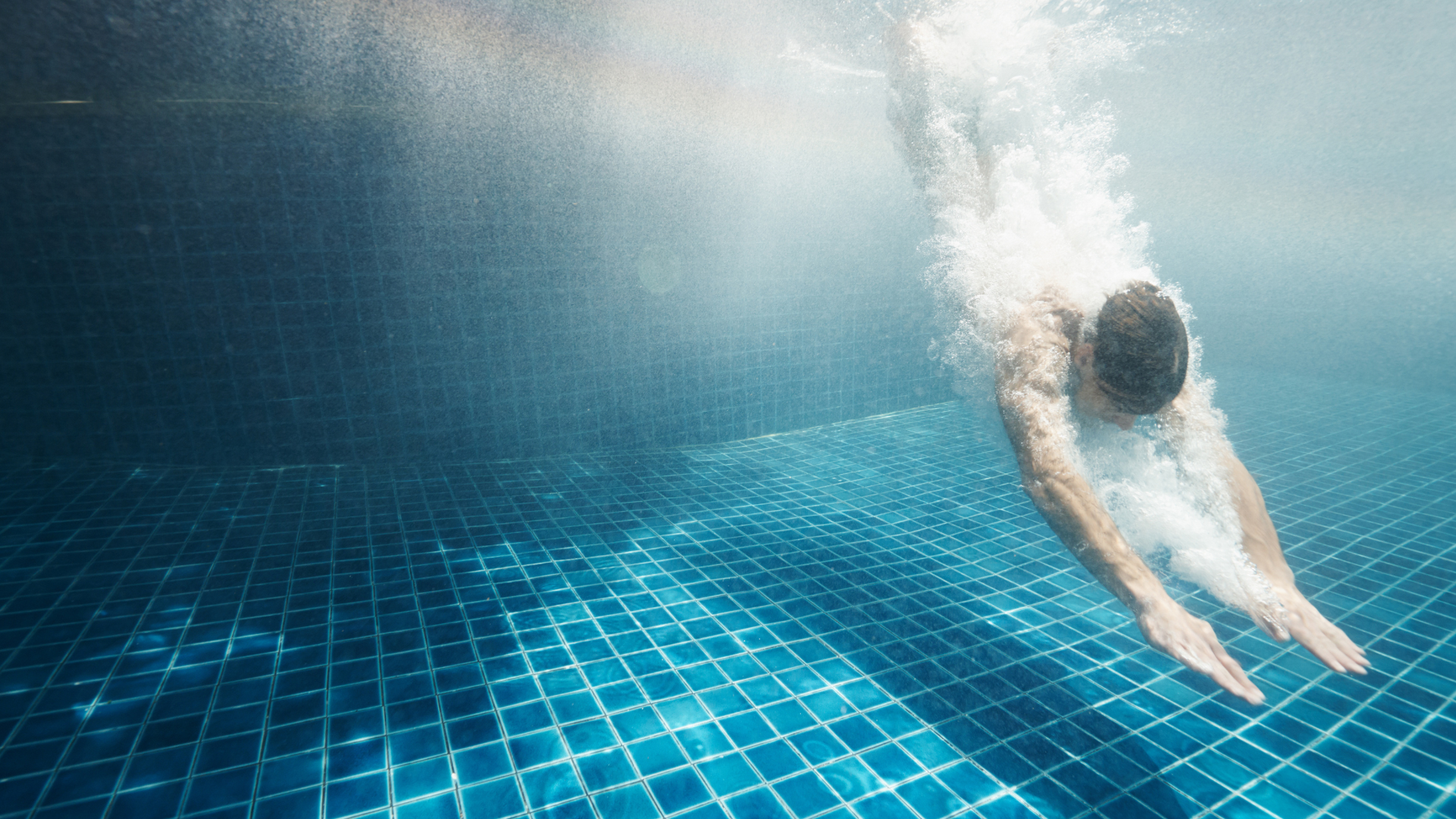 A man dives deep into a blue tiled swimming pool.